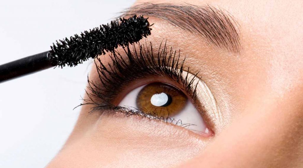 Woman applying mascara on eyelashes